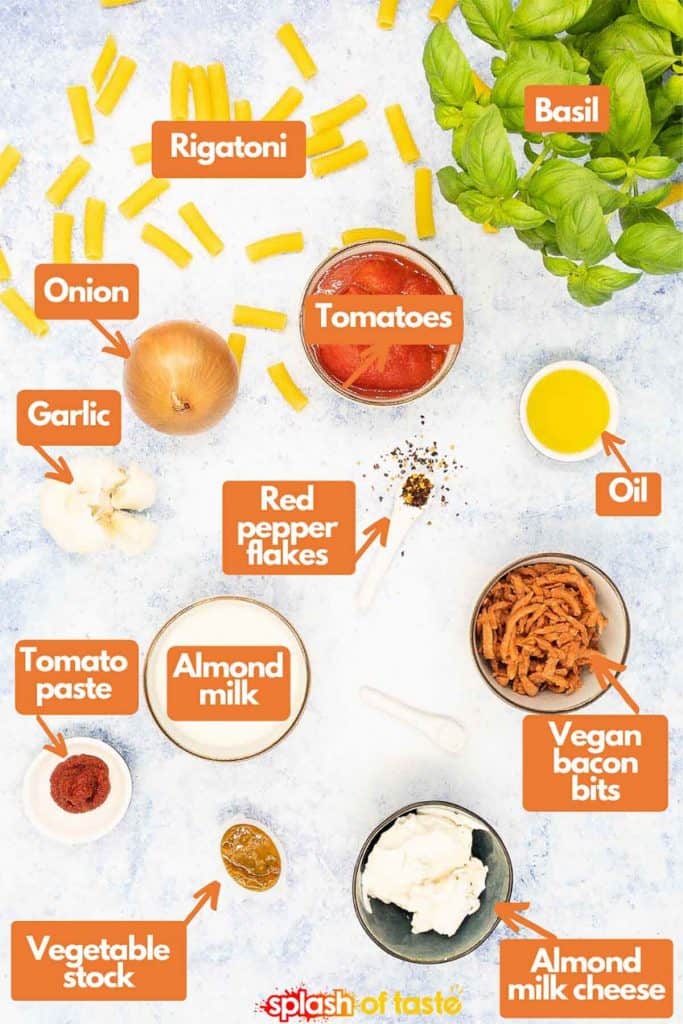 Ingredients for pink sauce pasta, rigatoni, fresh basil, olive oil, tomatoes, onion, garlic, red pepper flakes, tomatoes, almond milk, vegan bacon bits, almond milk cheese, vegetable stock and tomato paste.