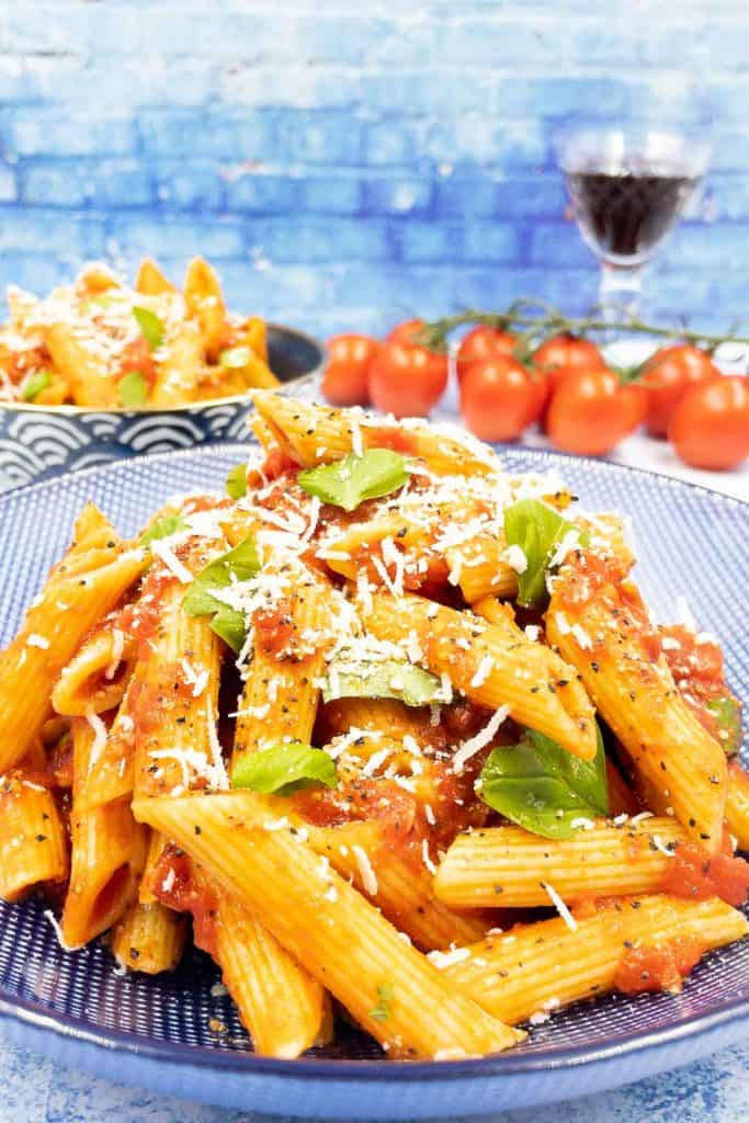 A bowl of homemade penne arribiata with fresh basil and Parmesan cheese.
