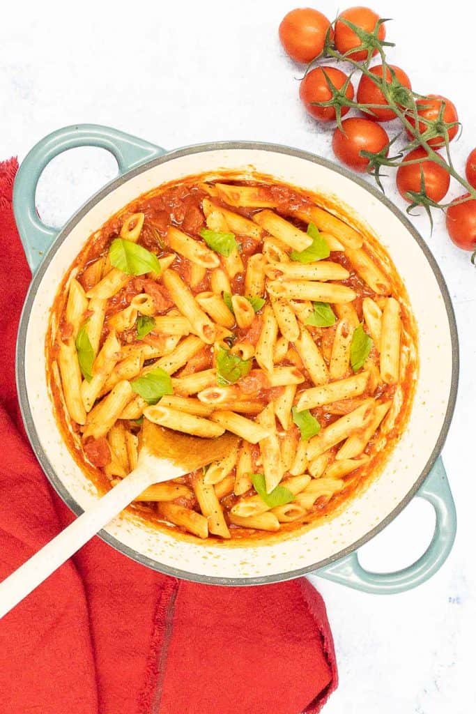 Penne arrabbiata in a pot with fresh basil and tomatoes.