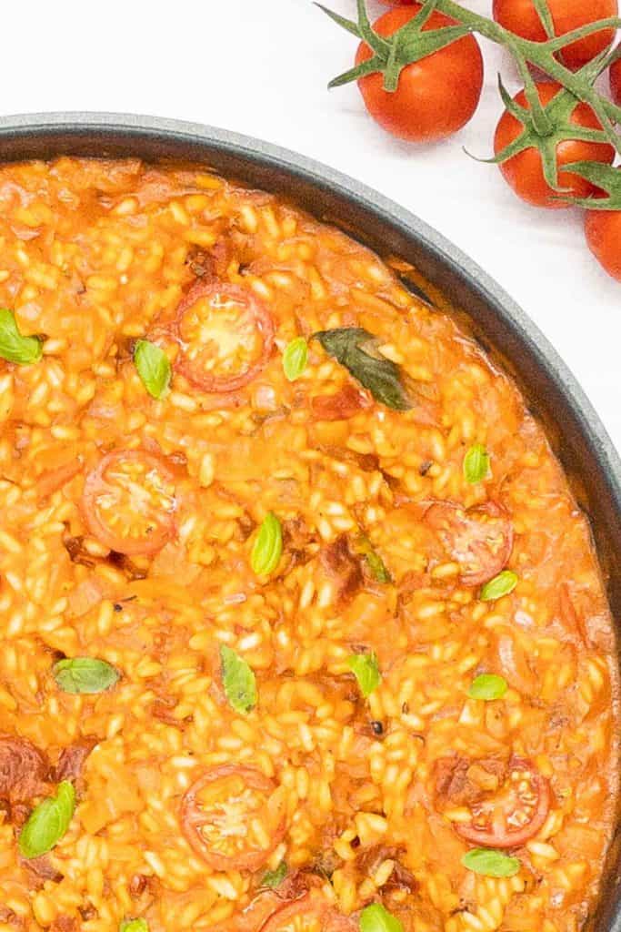 Creamy vegan risotto freshly made and in a pan, with fresh tomatoes on the vine.