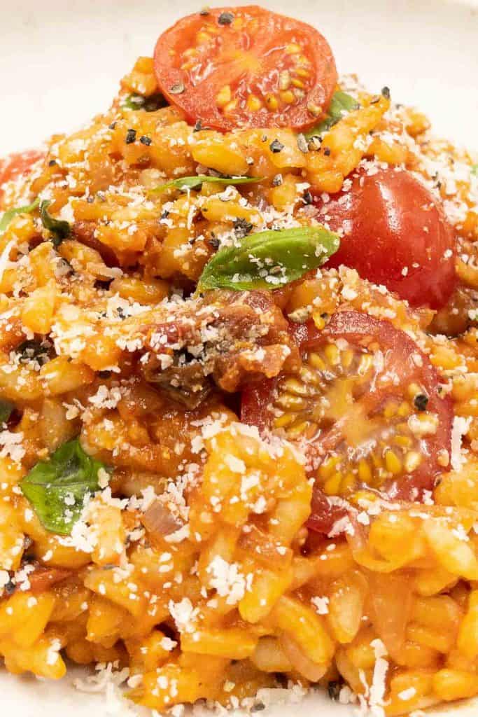 Close up of a bowl of tasty homemade creamy vegan risotto with cherry tomatoes, fresh basil and finely grated vegan Parmesan cheese.