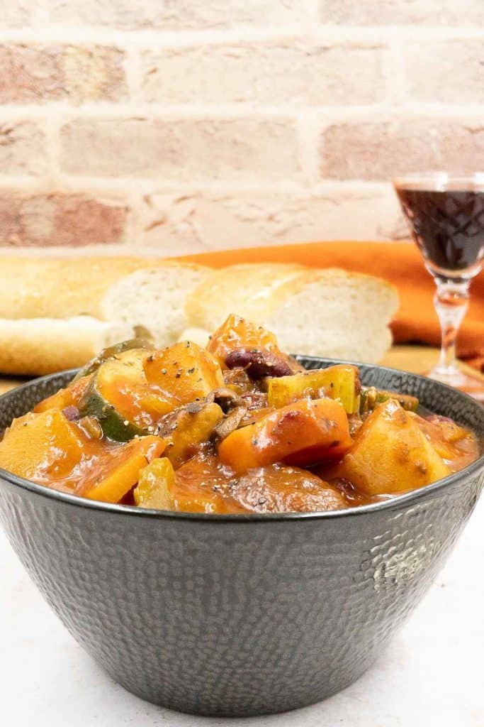 A freshly made bowl of hearty vegan stew, a glass of red wine and crusty bread.