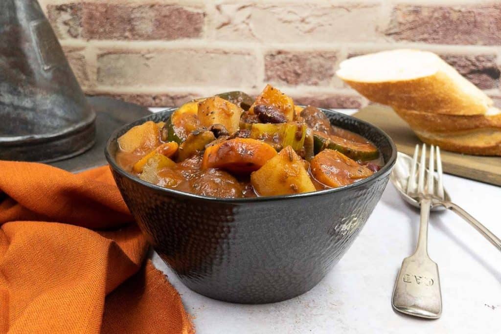 A bowl of hearty vegetable stew with crusty bread and a knife and fork.
