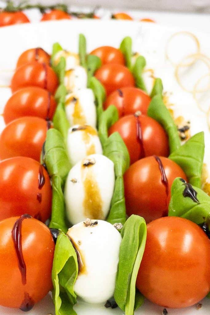 Close up of a line of freshly made Caprese skewers with a balsamic glaze and freshly ground black pepper.