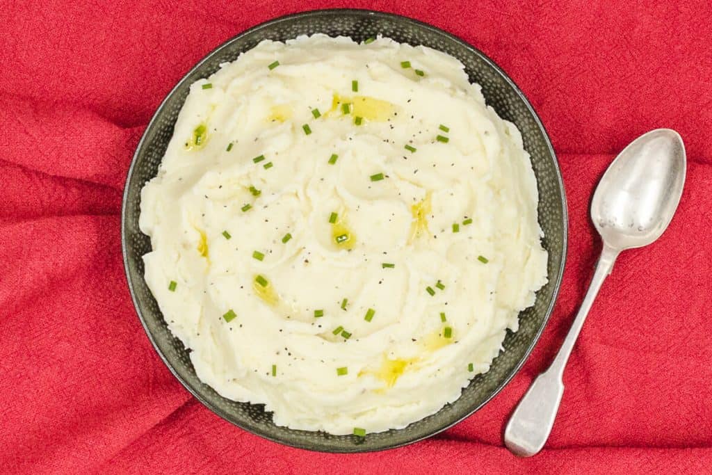 A bowl of homemade mashed potato with a serving spoon, ready to eat.