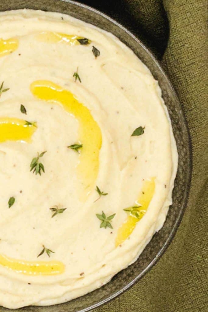 Close up of a bowl of creamy parsnip puree, with melted butter and fresh thyme garnish.