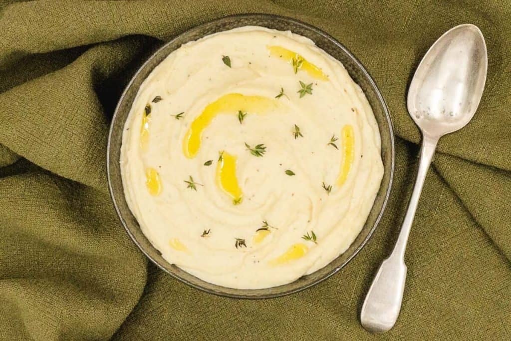 A bowl of delicious homemade parsnip puree, with olive oil and fresh thyme garnish,.