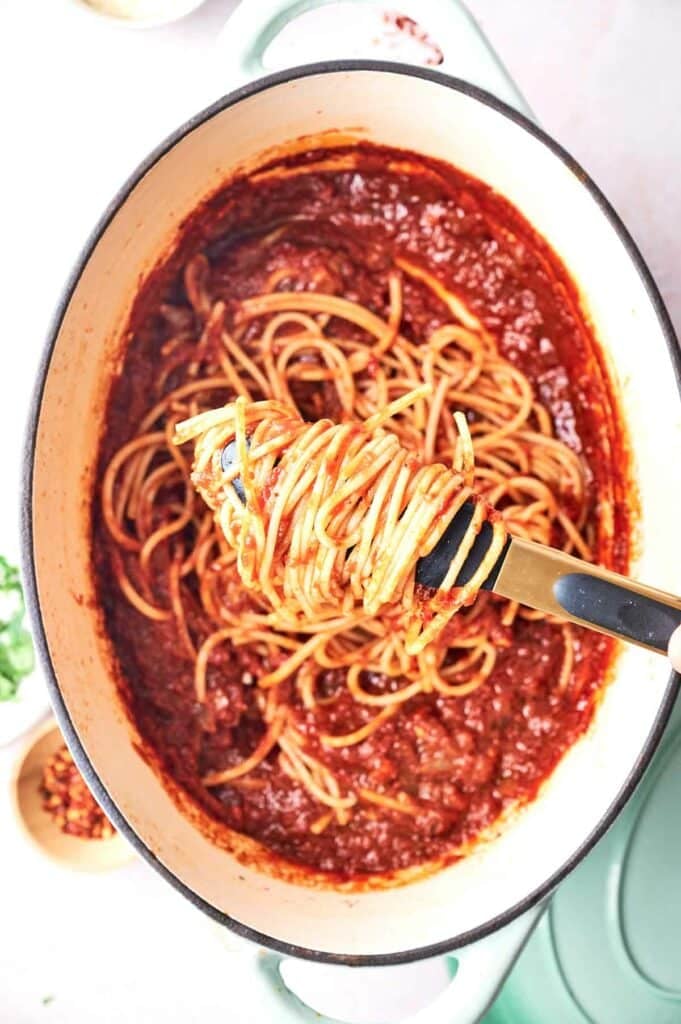 Spaghetti in a pot with a spoon, topped with marinara sauce.