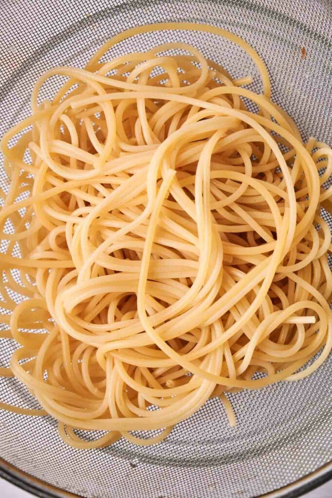 Cooked spaghetti drains in a fine mesh strainer, ready to be tossed with marinara sauce.