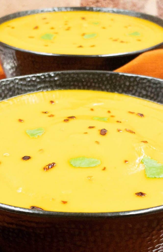 Creamy sweet potato soup in bowls with red pepper flakes and cilantro.