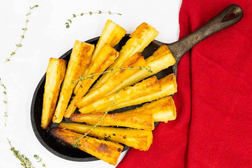 A dish of homemade roast parsnips, golden brown and ready to eat, with sprigs of fresh thyme.