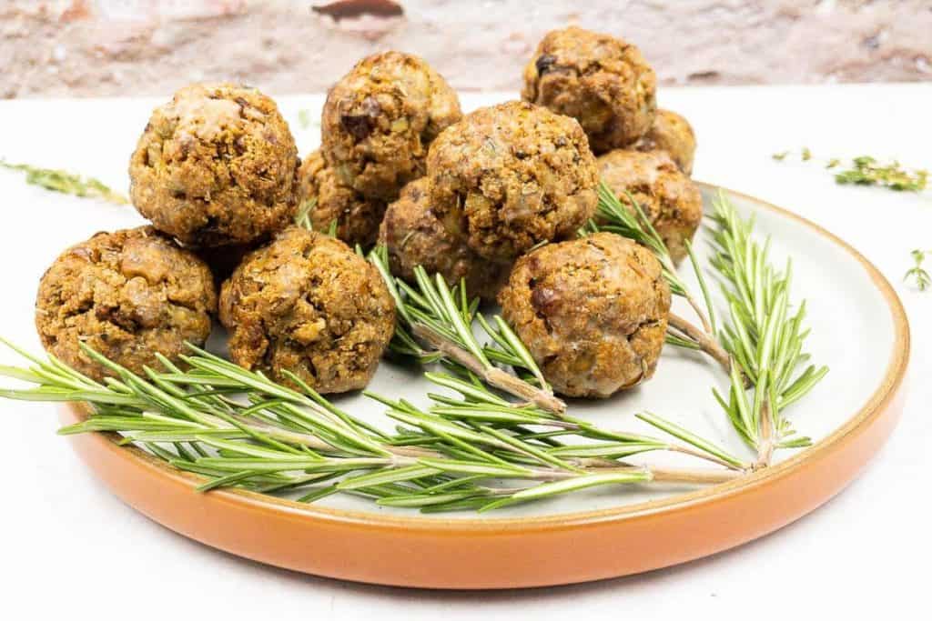 A plate of homemade thanksgiving stuffing balls with fresh rosemary and fresh thyme around it.