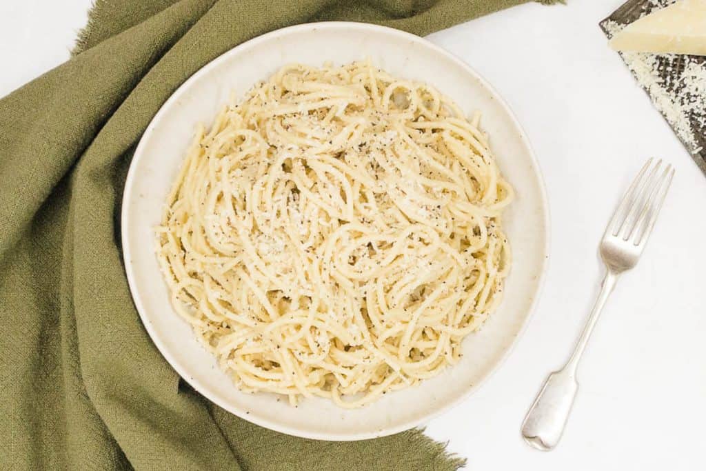 A bowl of tasty cacio e pepe with grated cheese and a fork to eat it with.