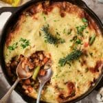 Vegetarian shepherd's pie in a skillet, topped with creamy mashed potatoes and garnished with fresh herbs. A portion is elegantly served with a silver spoon.