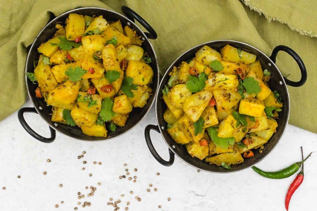 Two delicious bowls of homemade jeera aloo cumin potatoes, with cumin seeds, cilantro,red chillies