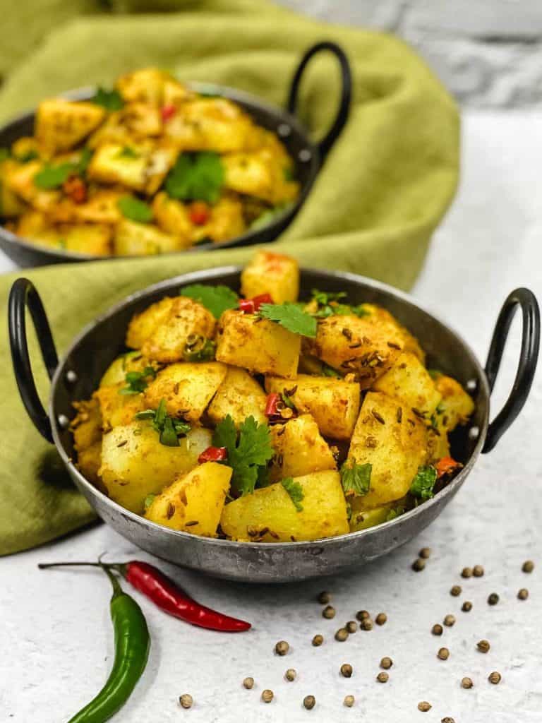 Delicious zeera aloo made from scratch in balti dishes, with red and green chilies and garnished with cumin seeds.