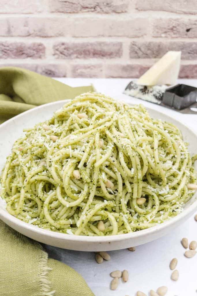 A side view of a pasta dish with spaghetti and a creamy sauce made from basil pesto.