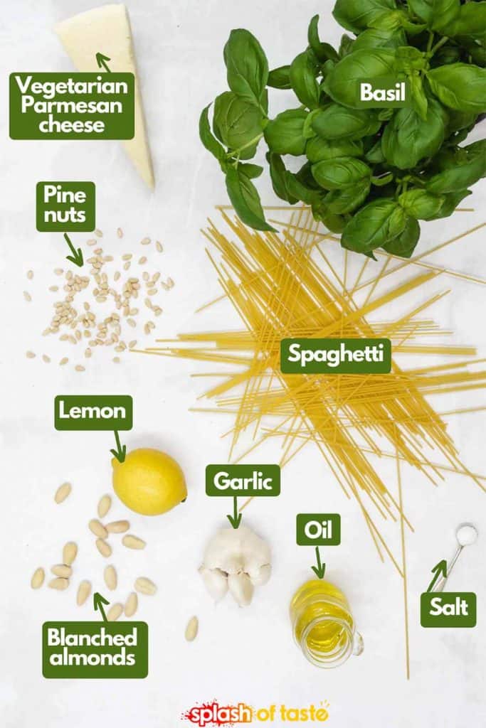 Ingredients needed to make pesto pasta, vegetarian Parmesan cheese, toasted pine nuts, fresh basil, spaghetti, lemon, garlic, olive oil, blanched almonds, salt and pepper.