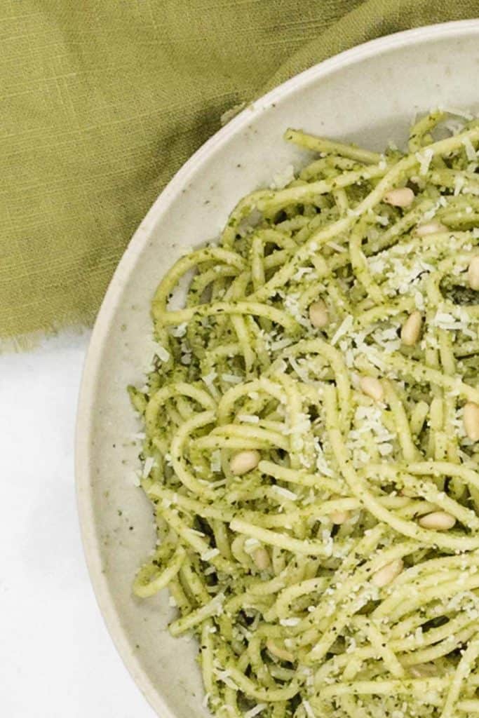 A close up of pesto pasta with toasted pine nuts and vegetarian grated Parmesan cheese.