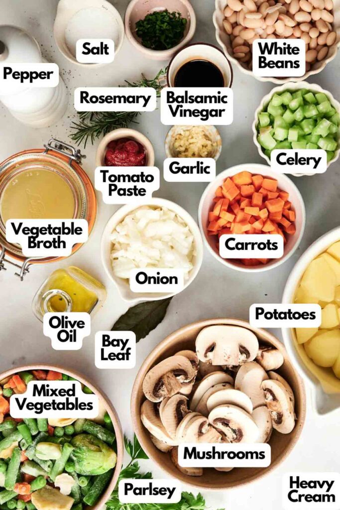 Ingredients for a cozy soup, reminiscent of a vegetarian shepherd's pie, featuring white beans, vibrant vegetables, an array of spices, olive oil, and heavy cream&mdash;all labeled individually on a light background.