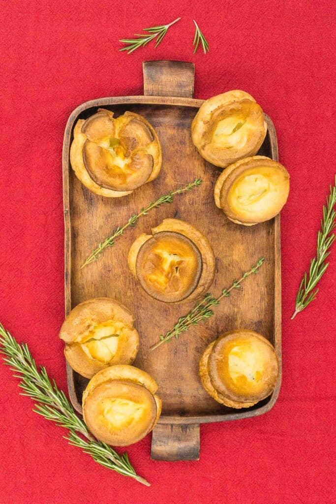 Overhead shot of gluten free Yorkshire puddings on a tray with fresh rosemary and thyme.