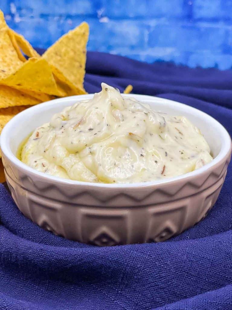 A delicious bowl of garlic and herb sauce, with tortillas in the background.