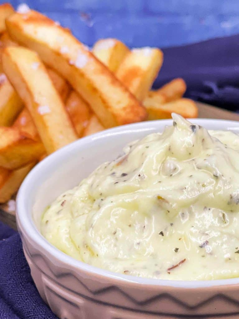 Close up of half a bowl of garlic dip with French Fries in the background.