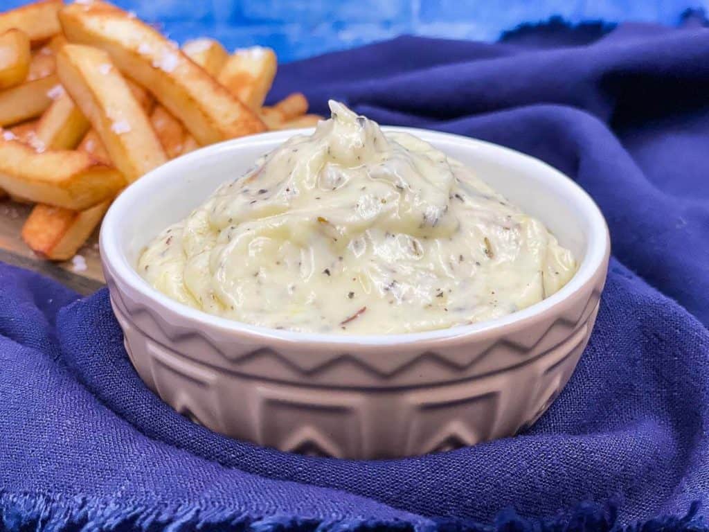 A bowl of homemade garlic dip with a plate of French fries.