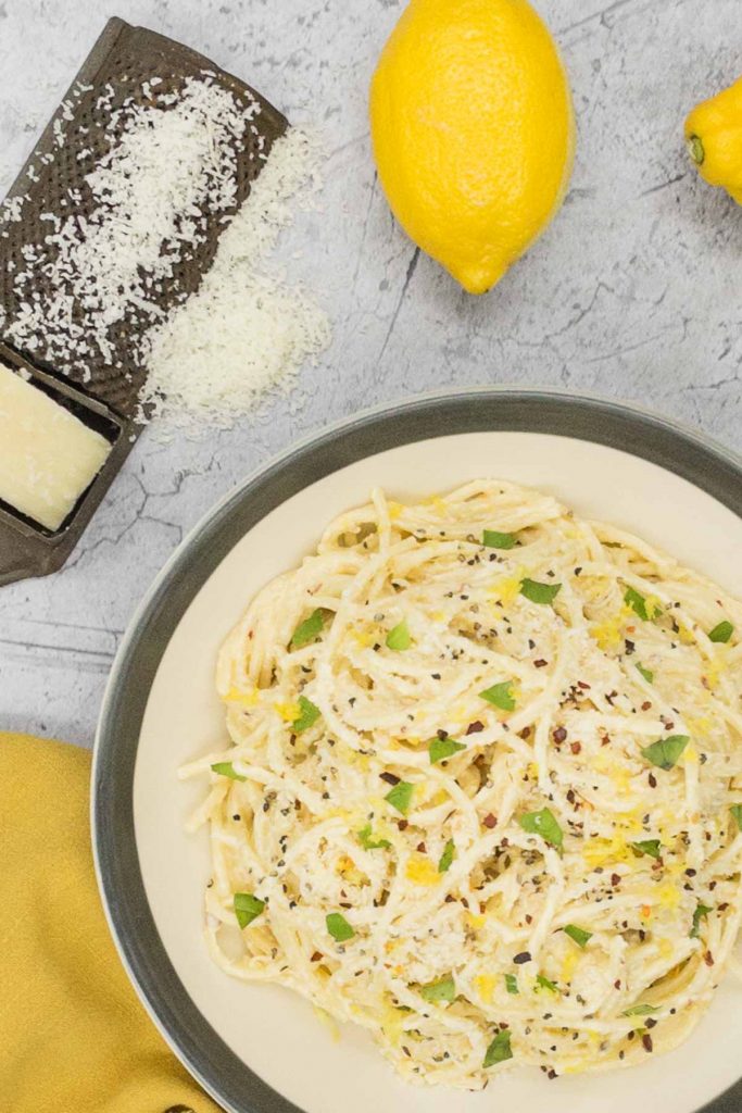 A bowl of freshly made lemon pasta, with a parmesan cheese grater and a fresh lemon.