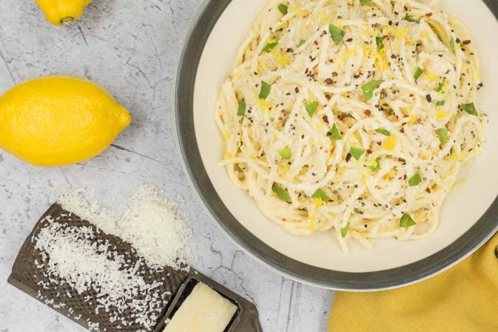 A bowl of freshly made lemon pasta, with a parmesan cheese grater and a fresh lemon.