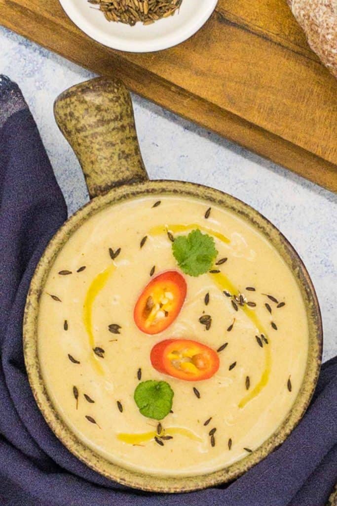 Freshly made soup made from parsnips, with red chili pepper slices, coriander leaves and cumin seeds on top of the soup.