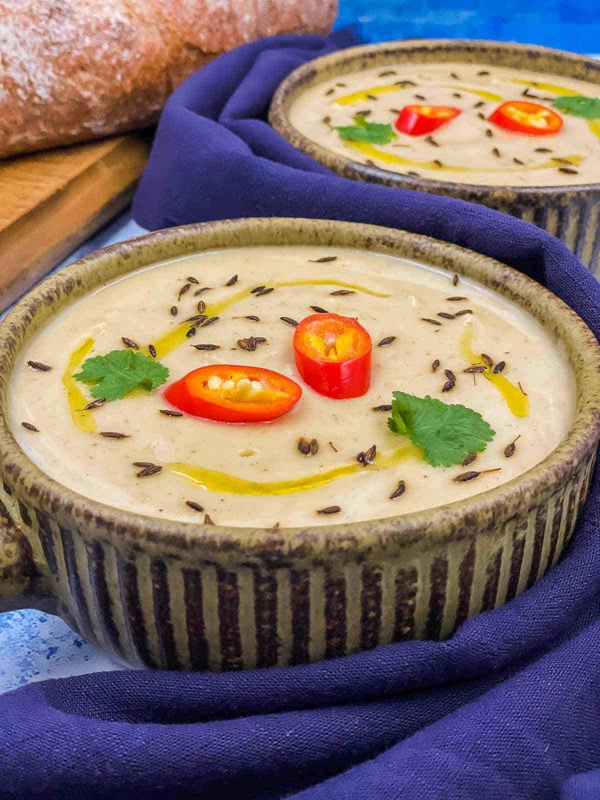 Two bowls of freshly made parsnip soup, with extra virgin olive oil, coriander leaves, red chili pepper slices and toasted cumin seeds.