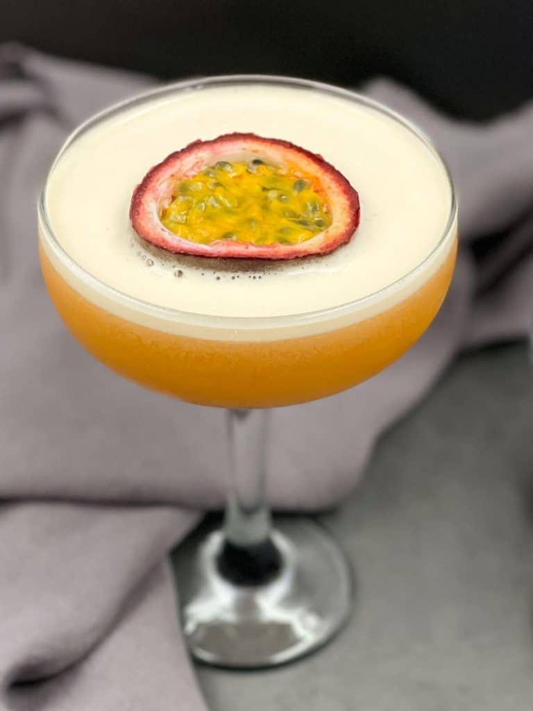 A passion fruit martini with half a passion fruit floating on the top of the foam.