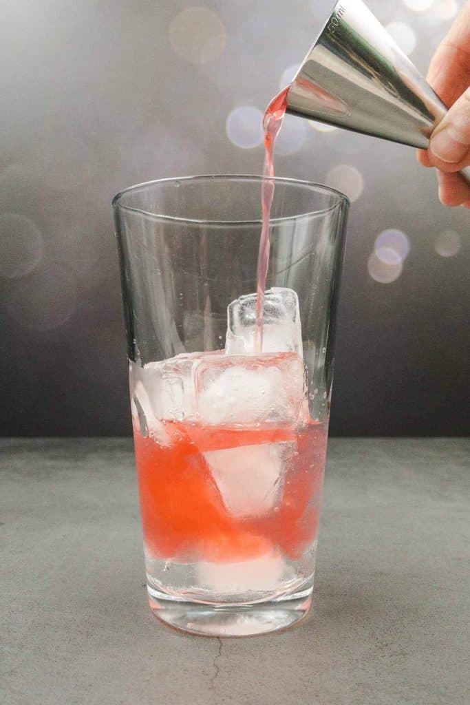 Pouring passion fruit liqueur into a cocktail shaker.