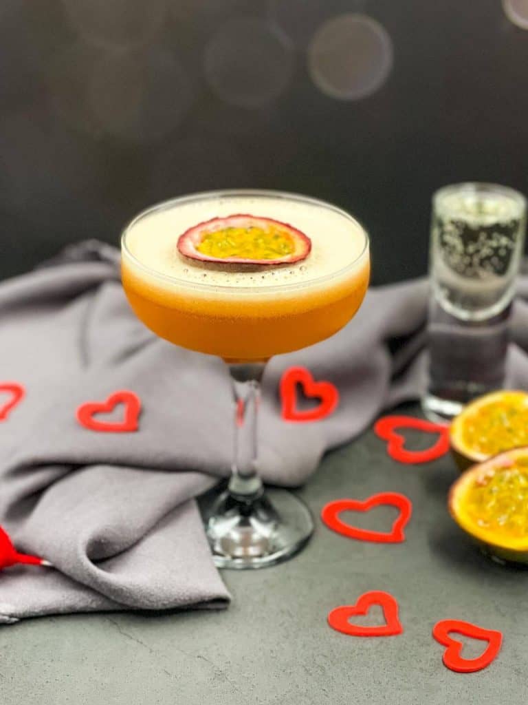 Passion fruit martini cocktail with a shot of prosecco, passion fruit halves and love hearts all around it.