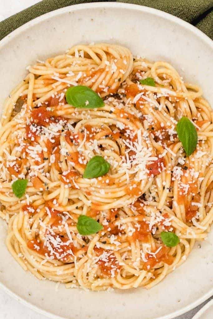 A bowl of spaghetti marinara, with grated Parmesan cheese on top with fresh basil.