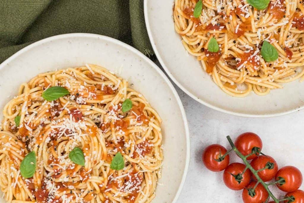 Two bowls of easy spaghetti marinara, ready to eat with fresh tomatoes on a vine.