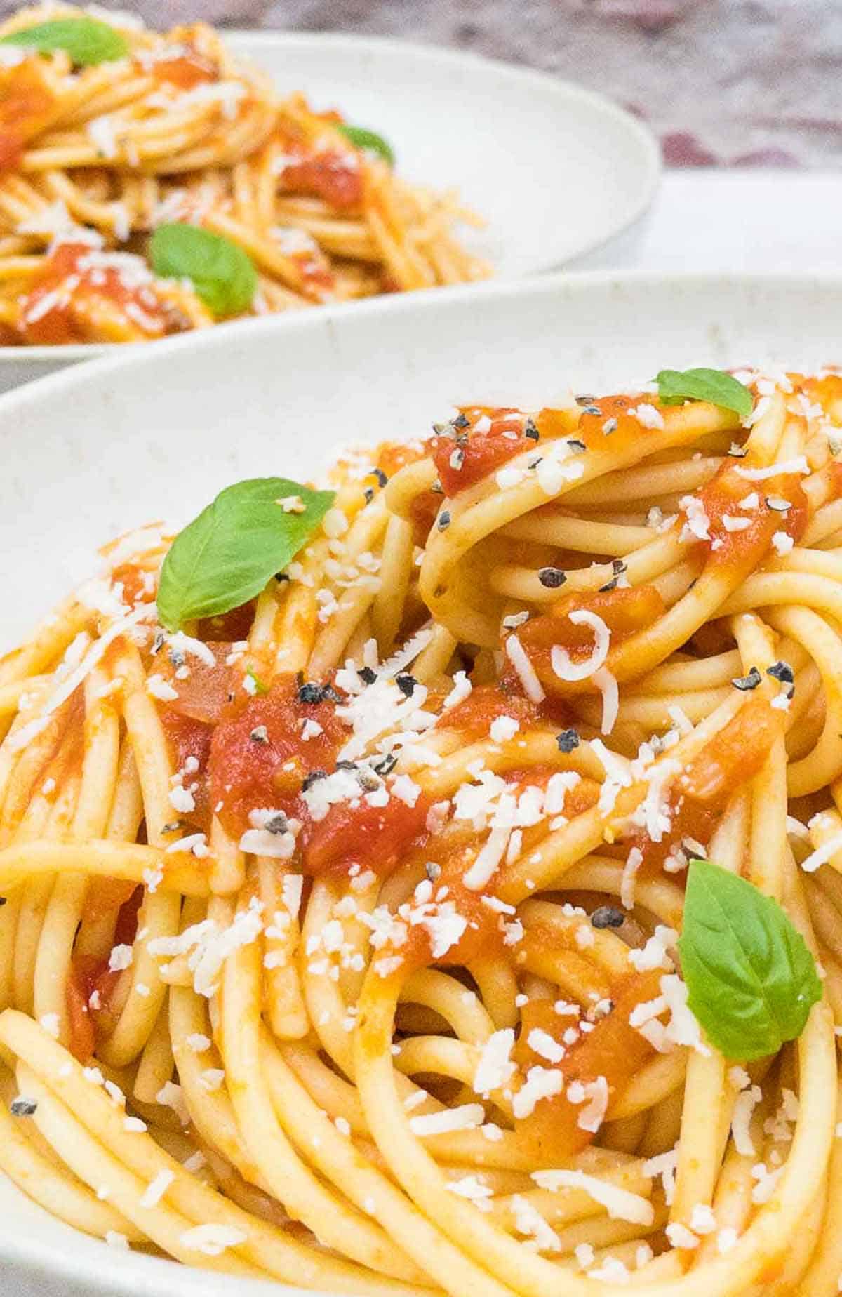 A bowl of spaghetti marinara with freshly grated Parmesan cheese and fresh basil.