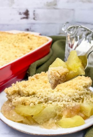 Homemade apple crumble in a baking dish with a portion served.