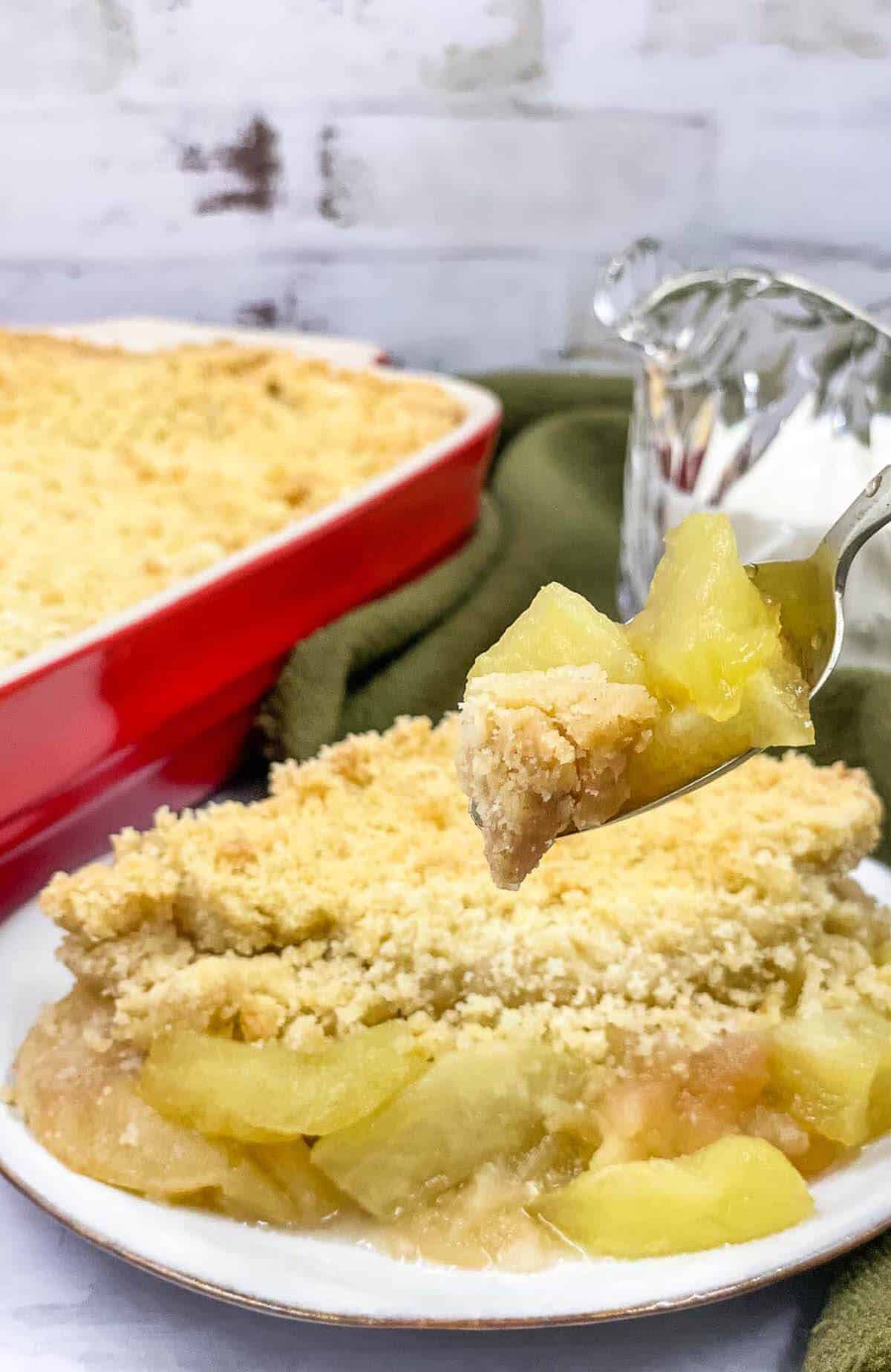 Homemade apple crumble in a baking dish with a portion served.