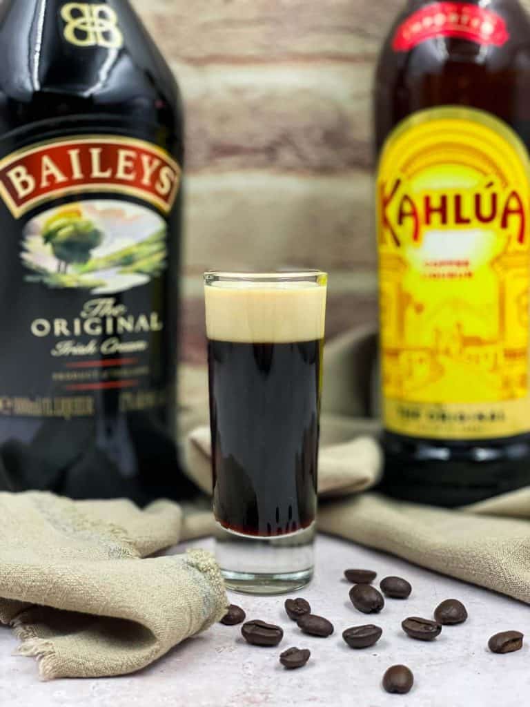 A shot of baby Guinness sitting in between two liqueur bottles, and coffee beans.