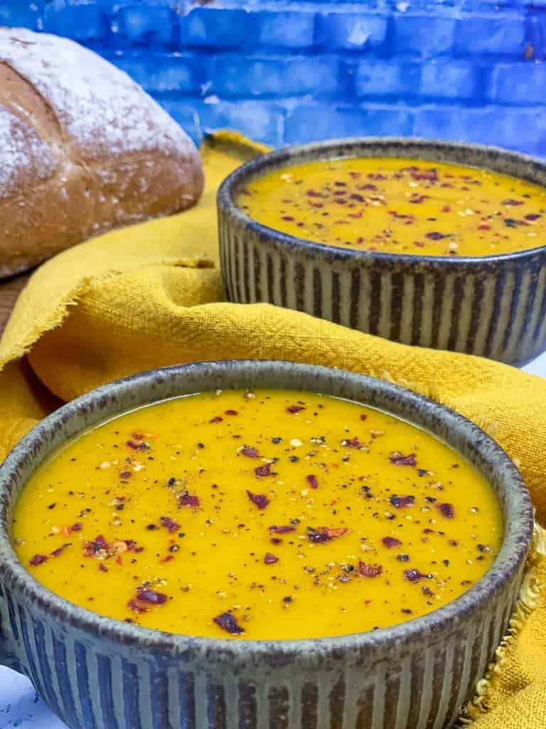 Bowls of freshly made carrot and parsnip soup, with yellow linen and fresh bread.