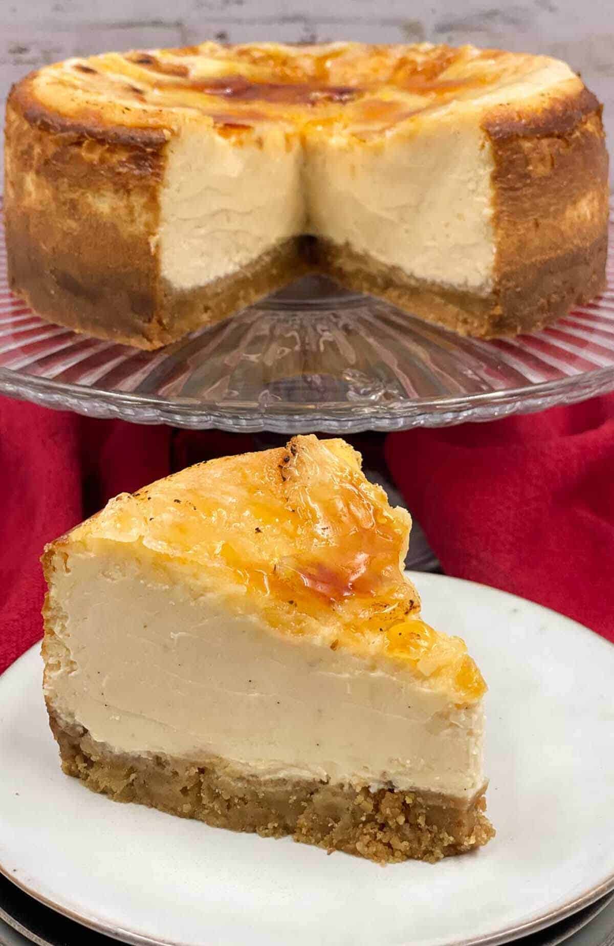 A slice of cheesecake made in creme brulee style and the cake it's come from on a stand behind.