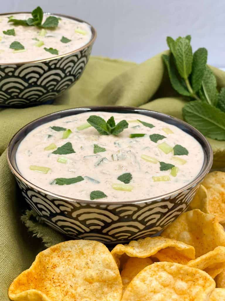 Two bowls of freshly made Indian cucumber raita with poppadoms, and mint.