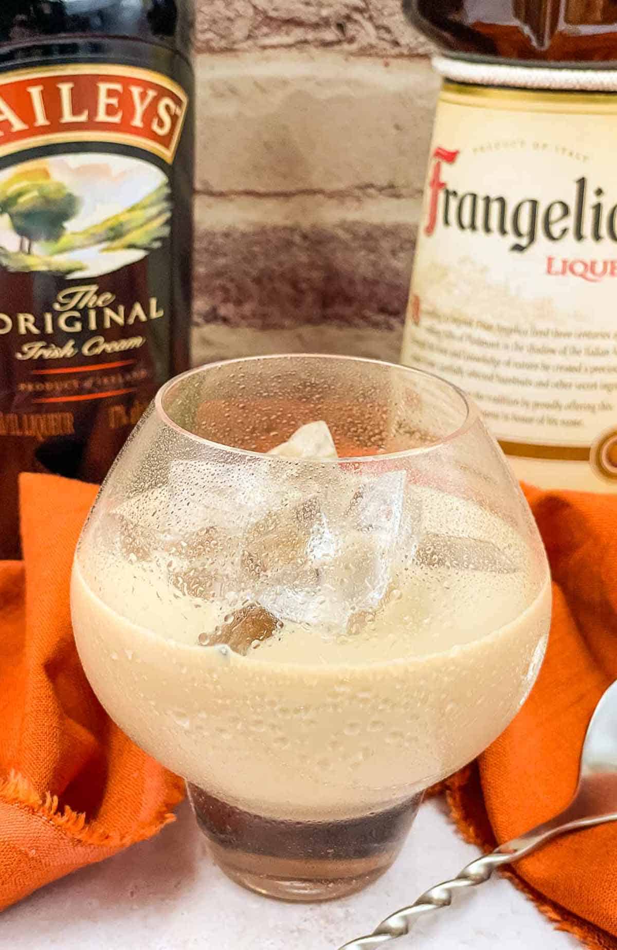 A glass of nutty Irishman on ice, with bottles of Baileys Irish cream and Frangelico liqueur in the background.