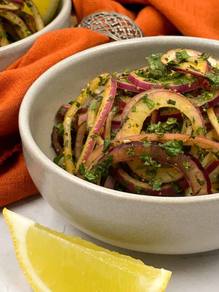 A bowl of red onion salad, with chopped mint and cilantro, and a lemon wedge.