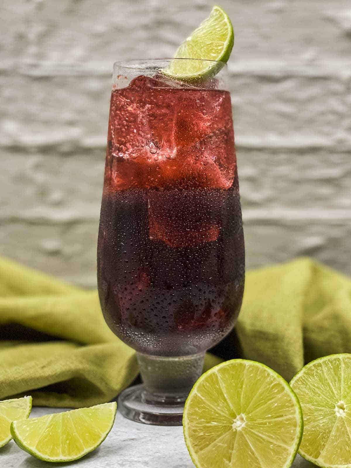 A purple rain cocktail freshly made with lime wedges and lime halves around it.