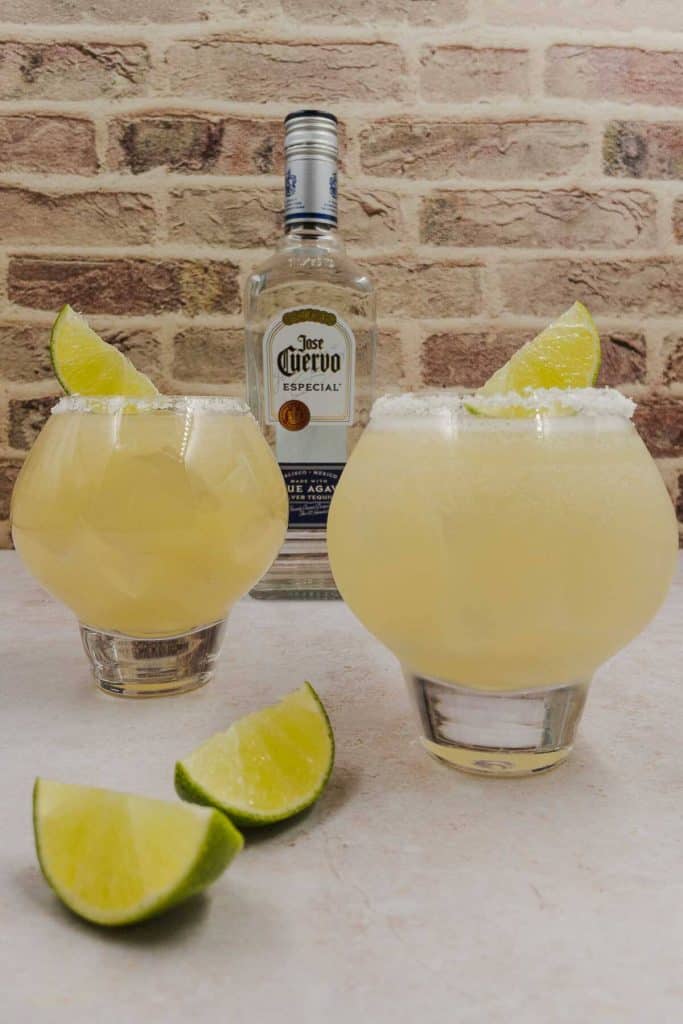 Two glasses of tequila grapefruit cocktail with lime wedges and a bottle of tequila in the background.