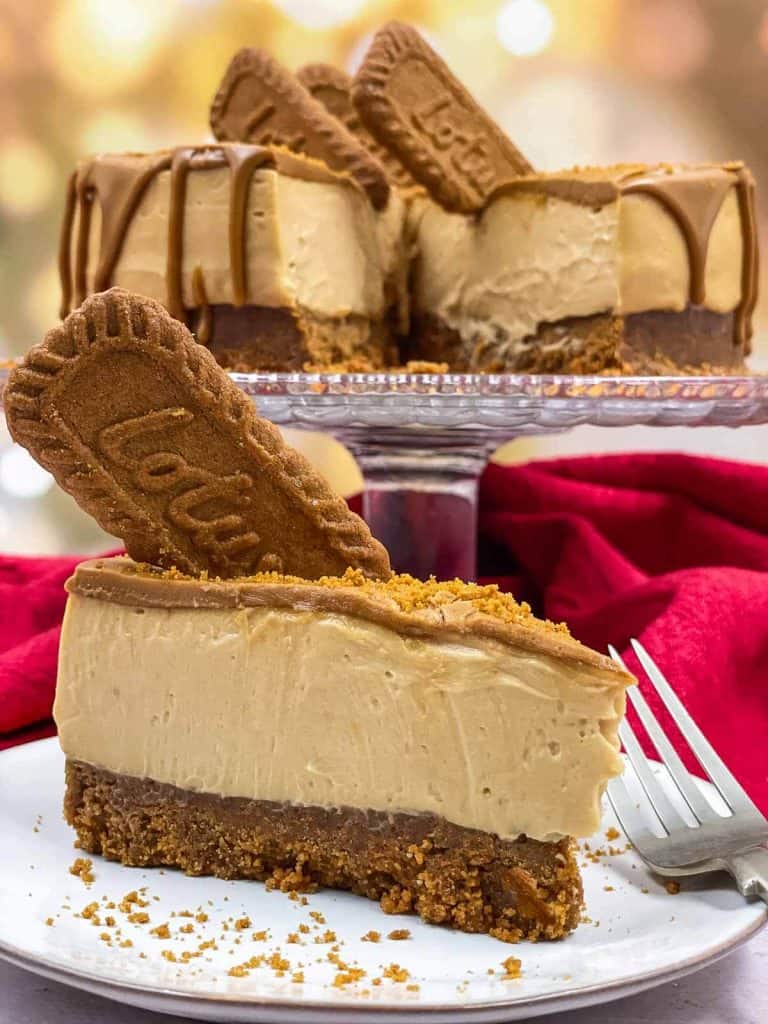 A vegan cheesecake on a cake stand with a slice missing that is on a plate ready to eat.