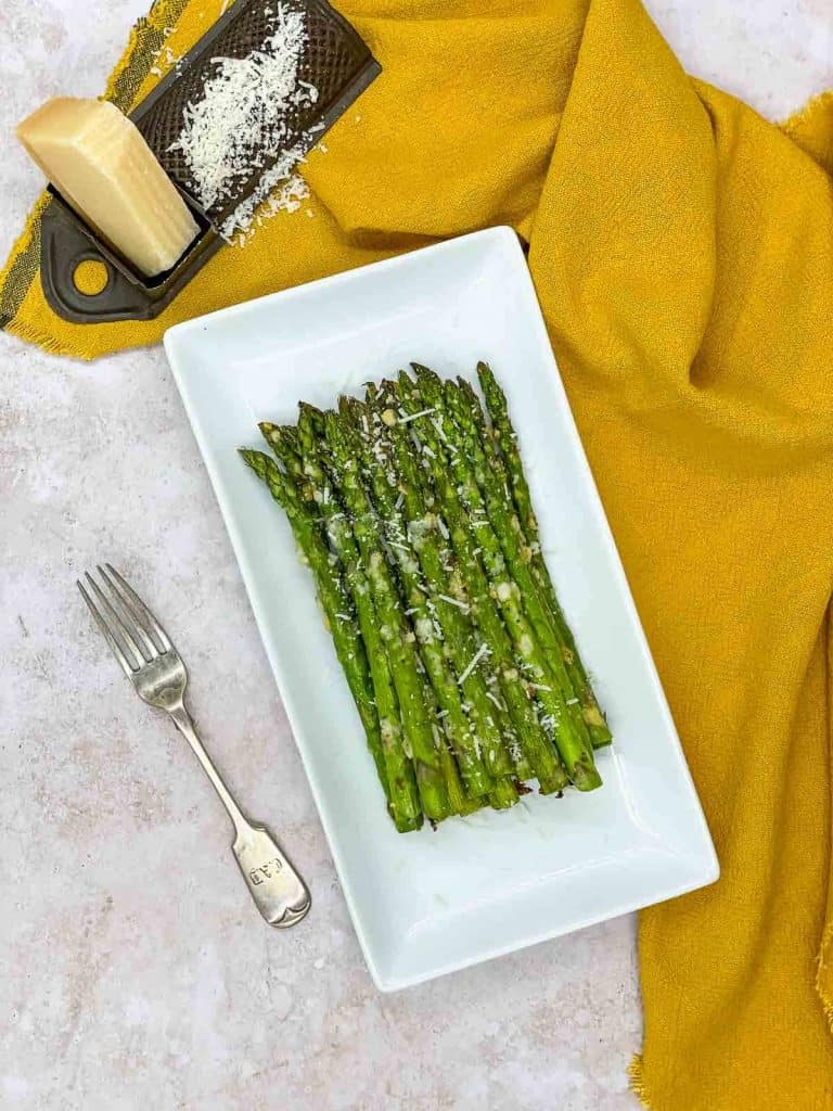A serving dishof freshly made air fryer asparagus, with Parmesan cheese and a fork.